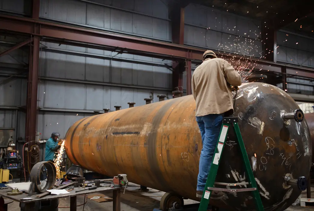 A man welding on a production separator indoors.